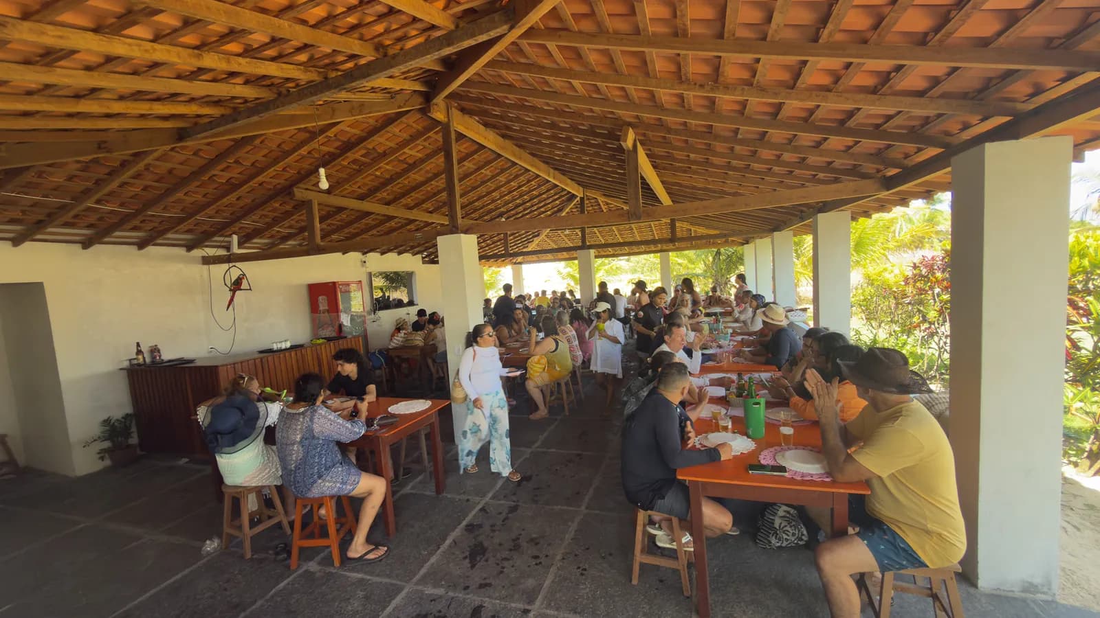 Salão coberto do Rancho Canto de Atins com mesas de madeira ocupadas por um grupo de turistas
